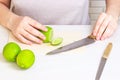 Fresh green sour lime cut with the knife on light wooden cutting board by woman hands in the kitchen. Royalty Free Stock Photo