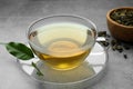 Fresh green tea in glass cup with saucer and leaves on grey table, closeup Royalty Free Stock Photo