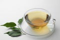 Fresh green tea in glass cup with saucer and leaves on white table Royalty Free Stock Photo