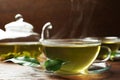 Fresh green tea in glass cup with saucer and leaves on wooden table, closeup Royalty Free Stock Photo