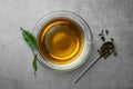 Fresh green tea in glass cup and spoon with dried leaves on grey table, flat lay Royalty Free Stock Photo