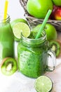 Fresh green vegetable smoothie in jar mug, fruit juice in bottle, scattered apples, lime, kiwi Royalty Free Stock Photo