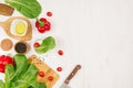 Fresh green vegetables, greens, red cherry tomatoes and kitchenware on soft white wood board, border, top view. Royalty Free Stock Photo