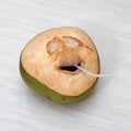 Fresh green young coconut with cut out smile and straw on wooden background