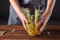 Woman`s hands hold pineapple halves with green leaves on a wooden brown table with copy space. Healthy product Royalty Free Stock Photo