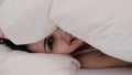 Fresh and happy brunette woman in bed at home. Beautiful girl hides under a blanket and smiling. Royalty Free Stock Photo