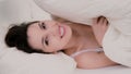 Fresh and happy brunette woman in bed at home. Beautiful girl hides under a blanket and smiling. Royalty Free Stock Photo