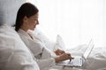 Woman lying in bed using laptop check email in morning