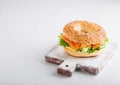 Fresh healthy bagel sandwich with salmon, ricotta and lettuce on vintage chopping board on stone kitchen table background. Healthy Royalty Free Stock Photo