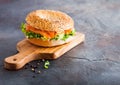 Fresh healthy bagel sandwich with salmon, ricotta and lettuce on vintage chopping board on stone kitchen table background. Healthy Royalty Free Stock Photo