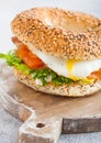 Fresh healthy bagel sandwich with salmon, ricotta and soft egg on vintage chopping board on white kitchen table background. Health Royalty Free Stock Photo