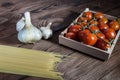 Fresh healthy cherry tomatoes, pasta spaghetti and garlic on wooden brown handmade cutting board