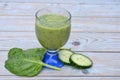 A fresh healthy green smoothie, cucumber slices, and a spinach leaf on a wooden table