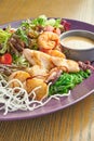 Fresh and healthy grilled seafood salad octopus, squid and shrimp, tomatoes and rice chips in a purple plate on a wooden