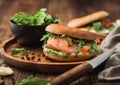 Fresh healthy organic sandwich with salmon and bagel, cream cheese and wild rocket in wooden plate with knife and linen towel