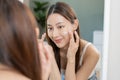 Fresh healthy skin, beautiful smile of asian young woman, girl looking at mirror, applying moisturizer on her face, putting cream Royalty Free Stock Photo