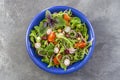 Fresh herb salad with leafy greens and nasturtium flowers served in blue ceramic bowl on grey