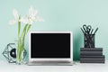 Fresh home workspace with blank laptop monitor, black stationery, books, abstract modern sculpture, white spring flowers in green. Royalty Free Stock Photo