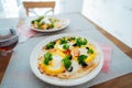 Fresh homemade breakfast pizza on bread wrap with eggs, cheese, tomatoes, bell pepper and herbs on the served table Royalty Free Stock Photo