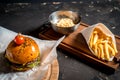 Fresh homemade burger on little cutting board with grilled potatoes, served with ketchup sauce and sea salt over wooden table with