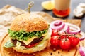 Fresh homemade burger on wooden board, pickles, sauce, cherry tomatoes and sliced onion. Side view, copy space Royalty Free Stock Photo