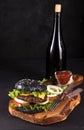 Fresh homemade burger on wooden serving board with fork and knife tomato sauce and vitage bottle on dark background Royalty Free Stock Photo