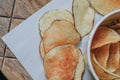 Fresh homemade deep fried crispy potato chips in white box on a wooden background, top view. Salty crisps scattered on a table for Royalty Free Stock Photo