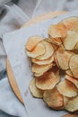 Fresh homemade deep fried crispy potato chips in white box on a wooden tray, top view. Salty crisps scattered on a table