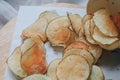 Fresh homemade deep fried crispy potato chips in white box on a wooden tray, top view. Salty crisps scattered on a table