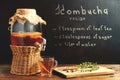 Fresh homemade kombucha fermented tea drink in a jar with faucet and in a cup and recipe on a dark wall