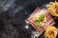 Fresh homemade pasta tagliatelle on wooden spoon with pasta ingredients tomatoes, raw egg, basil leaf on the dark concrete backgro Royalty Free Stock Photo