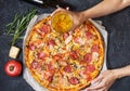 Fresh homemade pizza with pepperoni, ham, cheese. Female hands hold glass of beer on rustic stone background Royalty Free Stock Photo