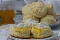 Close up of fresh scones topped with homemade apricot jam and whipped cream with jam jar and scones in background