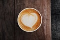 Fresh hot cappuccino coffee in a paper cup with beautiful latte art in the shape of heart on wooden background. Coffee to go. Royalty Free Stock Photo