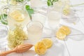Fresh iced lemonade with lemons and elderberry flowers in a jar and glasses on white tile table with hard shadows