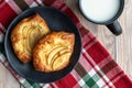 Fresh individual apple tarts on a black plate, cup of milk, red, green, and white cloth napkin, wood background Royalty Free Stock Photo