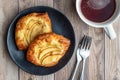 Fresh individual apple tarts on a black plate, forks, cup of hot tea, wood background Royalty Free Stock Photo