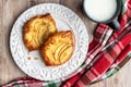 Fresh individual apple tarts on a white plate, cup of milk, red, green, and white cloth napkin, wood background Royalty Free Stock Photo