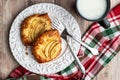 Fresh individual apple tarts on a white plate with forks, cup of milk, red, green, and white cloth napkin, wood background Royalty Free Stock Photo