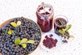 Fresh juice and jam of black chokeberry Aronia melanocarpa in glass and berry in pot on white textured background