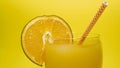 Fresh juice with a slice of orange on a glass and a straw, a summer drink on a bright yellow background, a close-up of orange Royalty Free Stock Photo