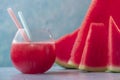 Fresh juice of sweet spanish watermelon in glass with straws and just cutted slices on blue background. Close up shot with Royalty Free Stock Photo