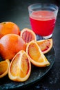 Fresh Juicy Blood Oranges Whole and Sliced on Dark Plate with Glass of Juice in Background Royalty Free Stock Photo