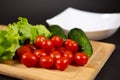 Fresh and juicy cherry tomatoes, cucumbers, gherkins, and lettuce leaves with water drops on a wooden cutting Board. Royalty Free Stock Photo