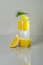 Fresh juicy lemon cut in cubes stacked on top of each other with ice cube in middle, slice of lime and rosemary branch