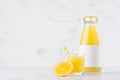 Fresh juicy orange juice in glass bottle with blank label mock up with wine glass decorated straw, fruit slices in soft light.