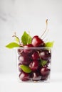 Fresh juicy red cherries in plastic container with green leaves, tails in sunlight as summer healthy food on modern white kitchen. Royalty Free Stock Photo