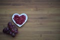 Food photography image of healthy red pomegranate seeds in a white love heart shape dish with purple grapes on wood background