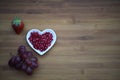 Food photography image of healthy red pomegranate seeds in a white love heart shape dish with a strawberry on wood background Royalty Free Stock Photo