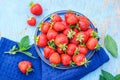 fresh juicy strawberries in a blue plate on an old wooden rural table, next to it is a dark blue napkin and mint leaves Royalty Free Stock Photo